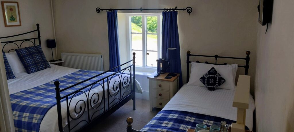 A hotel room with a double and single bed. blue checked blankets