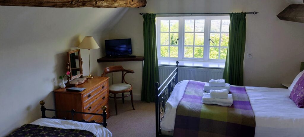 a hotel room with a double and single bed. greenery visible through the window