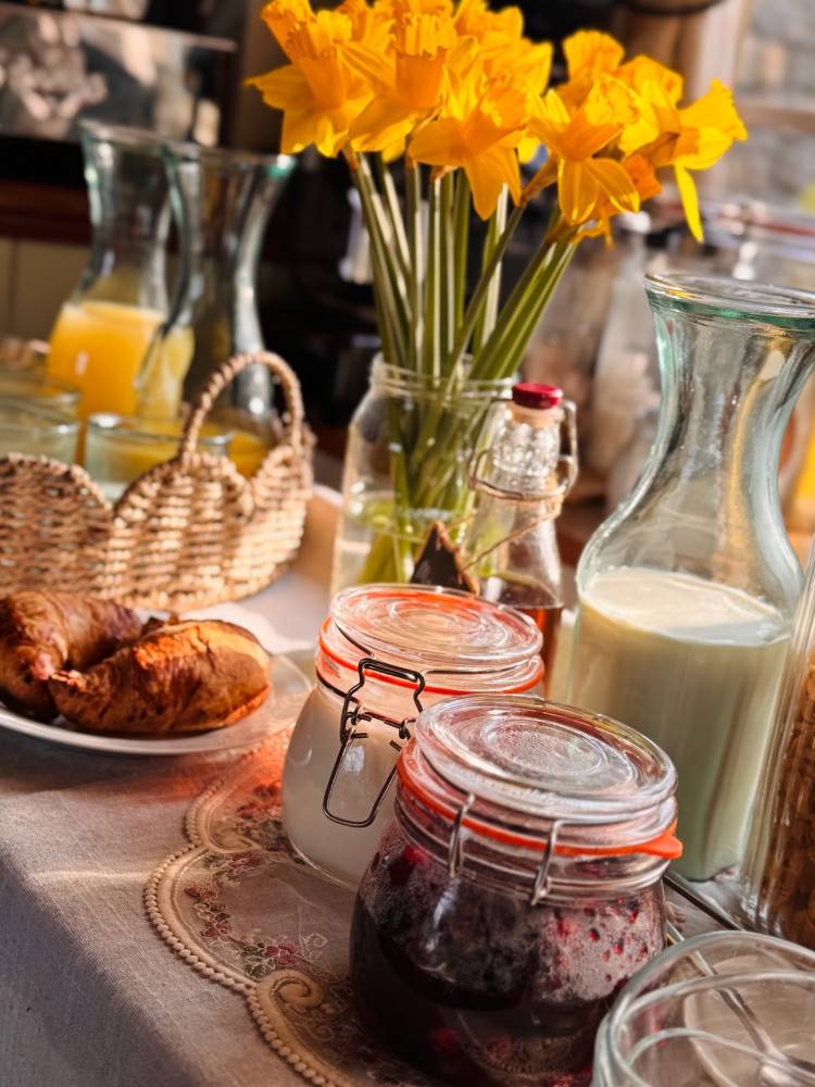 A table set for breakfast with milk, juice, jam and pastries. A vase of yellow daffodils